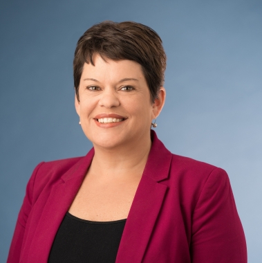 Headshot of a woman with a brown pixie cut, smiling, wearing a red blazer.